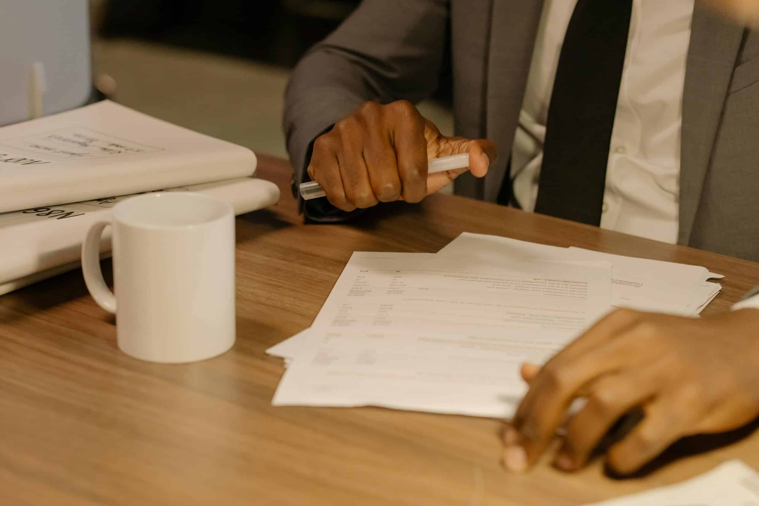 Free Close-up of a businessman holding and reviewing documents on a wooden desk. Stock Photo